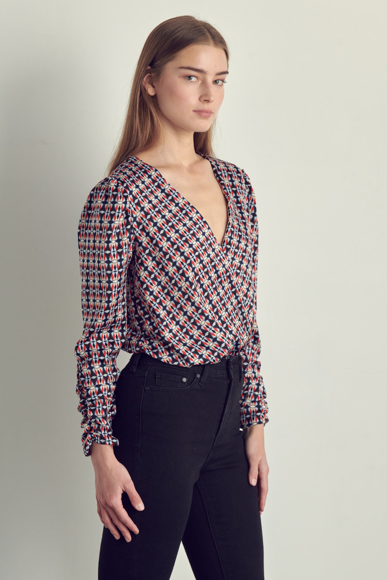 Ruched long sleeve surplice bodysuit in satin abstract print, featuring a stylish neckline and ruched cuffs.