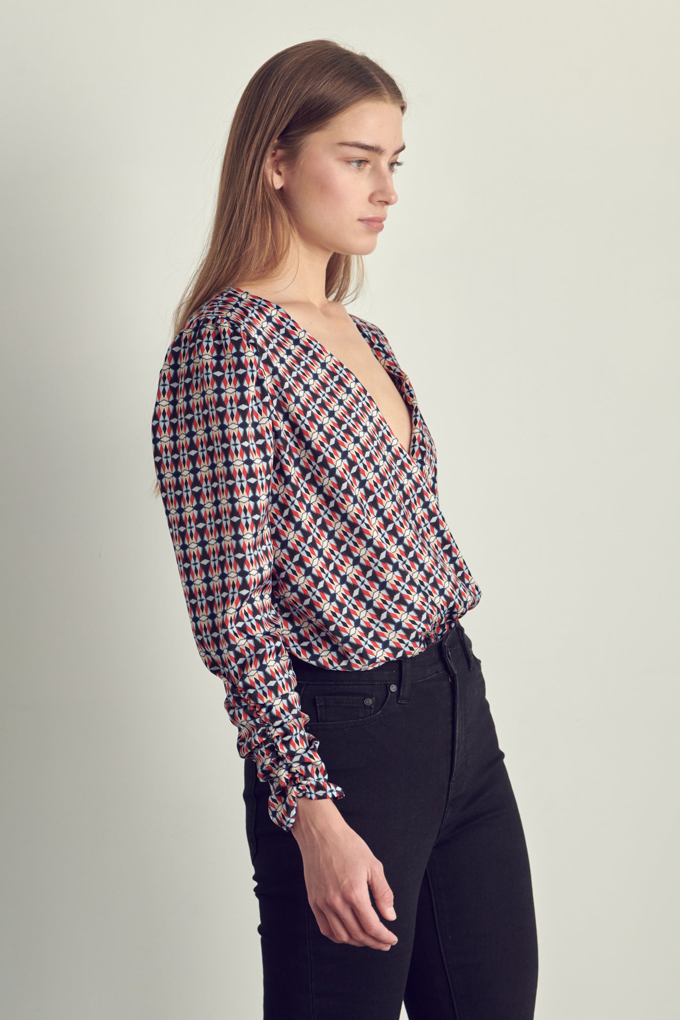 Ruched long sleeve surplice bodysuit in satin abstract print, featuring a stylish neckline and ruched cuffs.