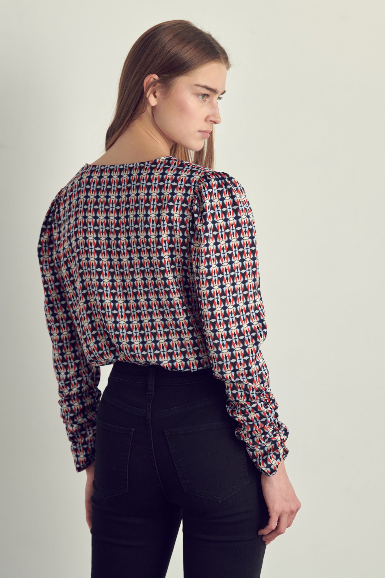 Ruched long sleeve surplice bodysuit in satin abstract print, featuring a stylish neckline and ruched cuffs.