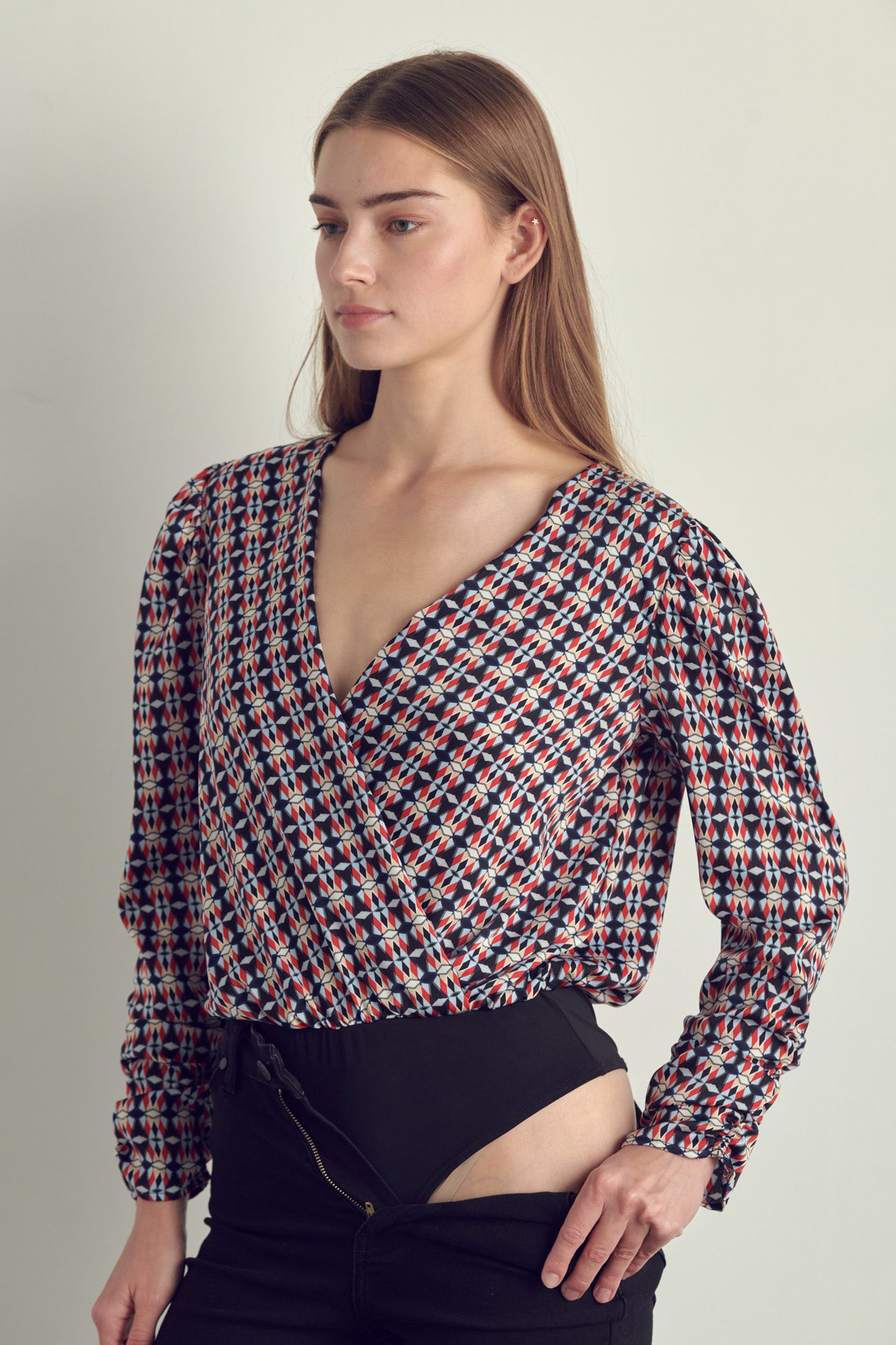 Ruched long sleeve surplice bodysuit in satin abstract print, featuring a stylish neckline and ruched cuffs.