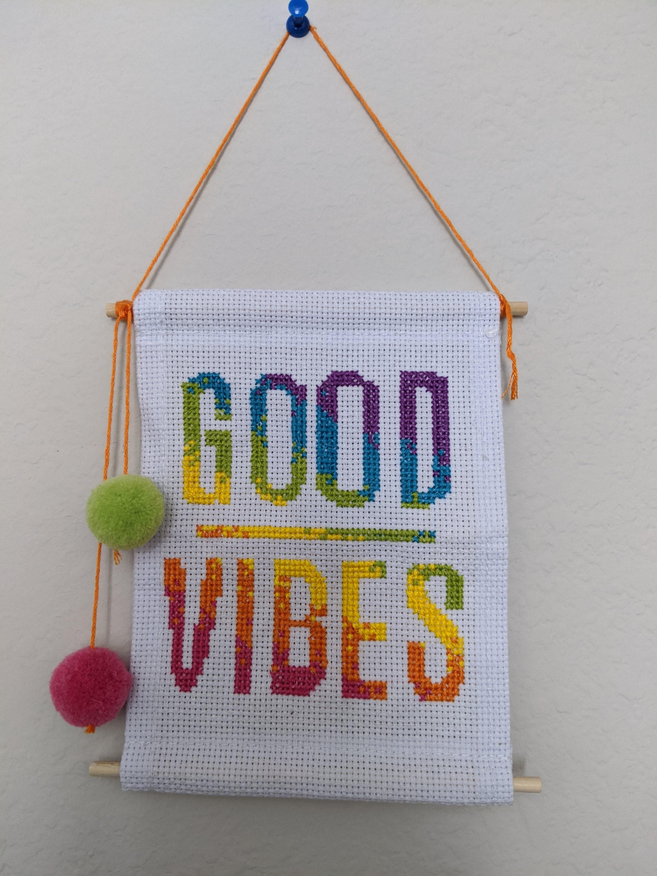 A colorful handmade cross stitched wall hanging featuring the words 'Good Vibes' in a cheerful design, perfect for teen and tween rooms.