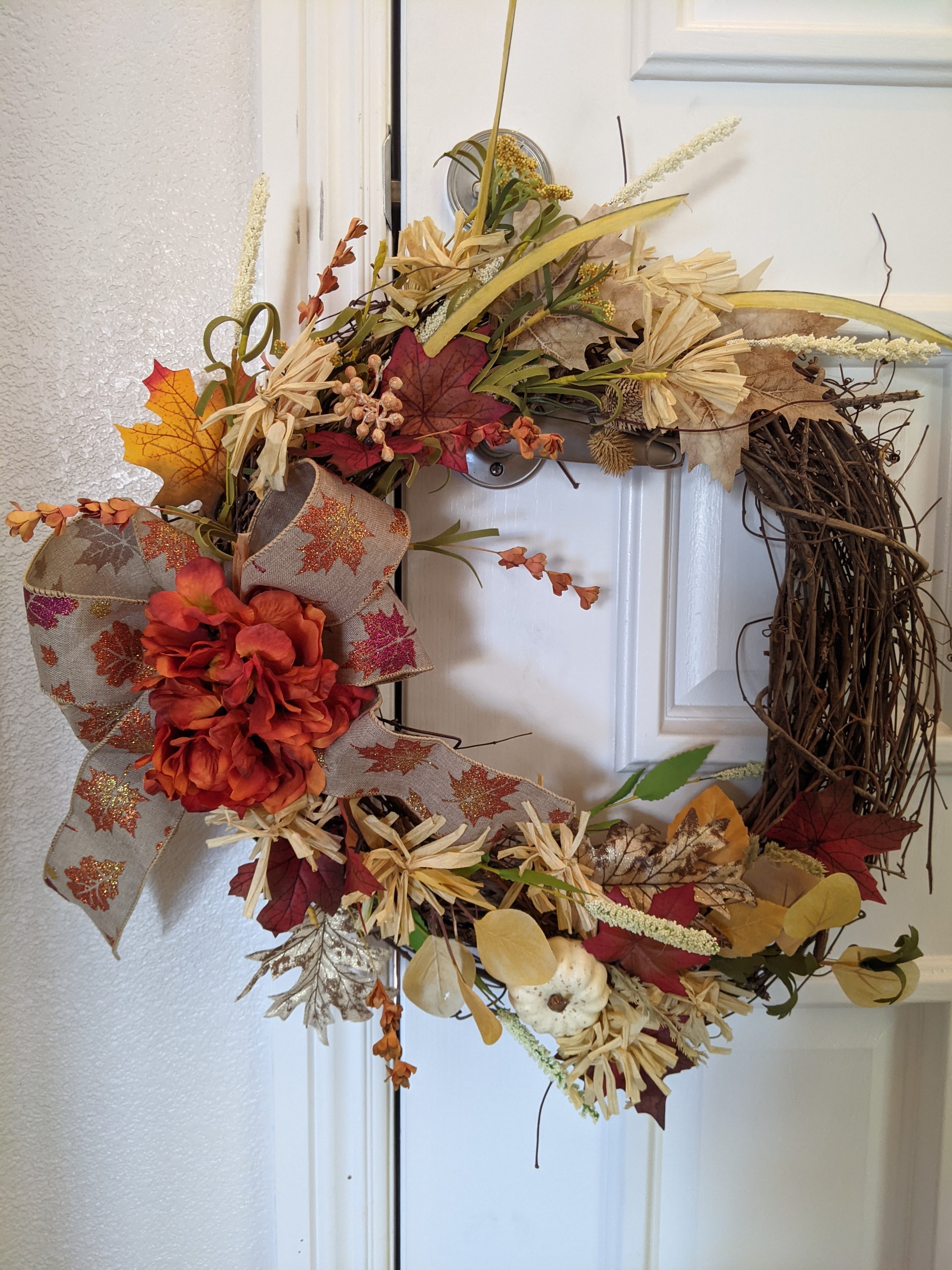 Handmade fall grapevine wreath featuring ivory, yellow, burgundy, and rust colors with a metallic bow and leaves.