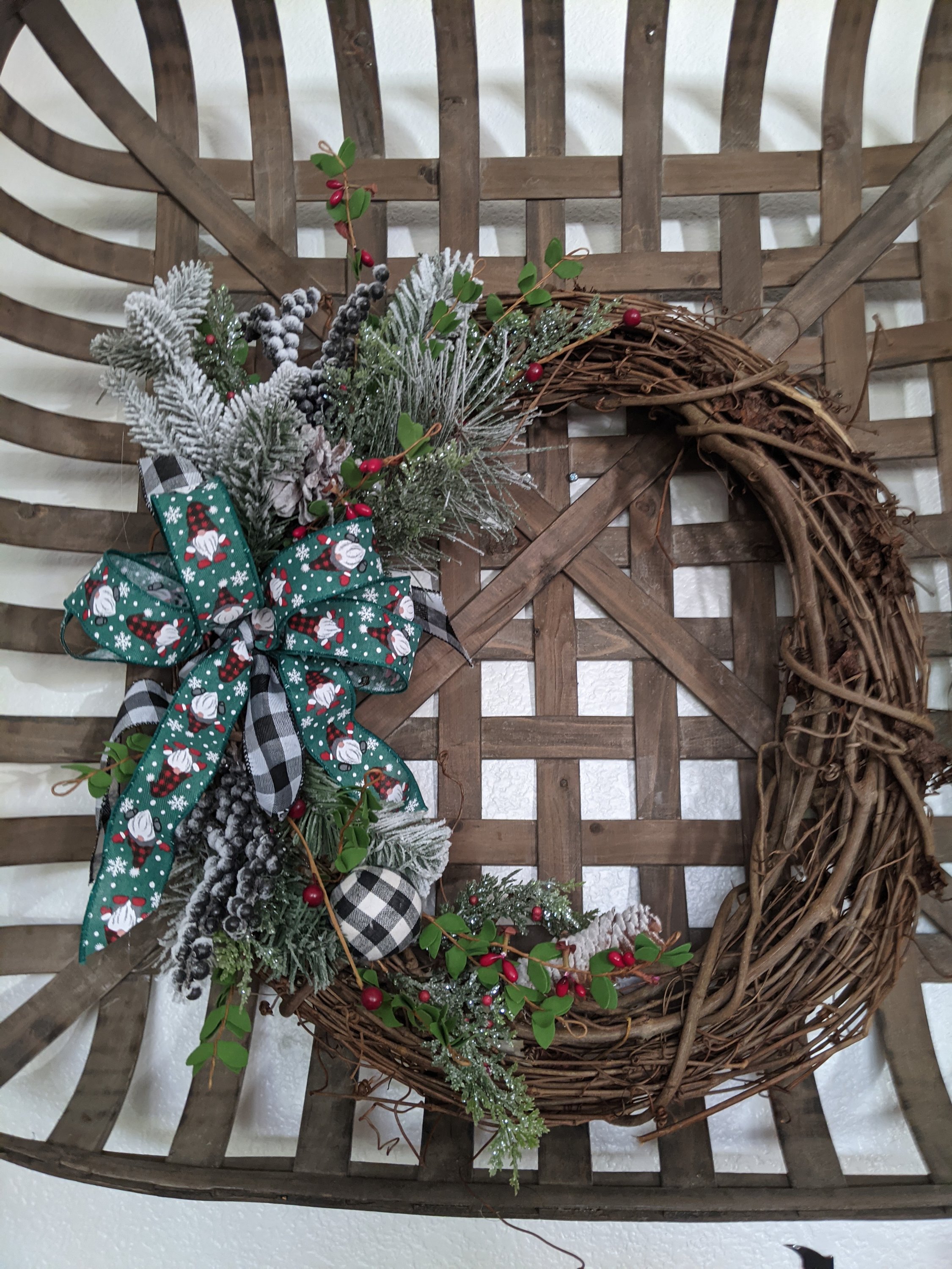 A handmade 18-inch grapevine wreath featuring gnome accents, buffalo plaid, and greenery, perfect for winter and Christmas decor.