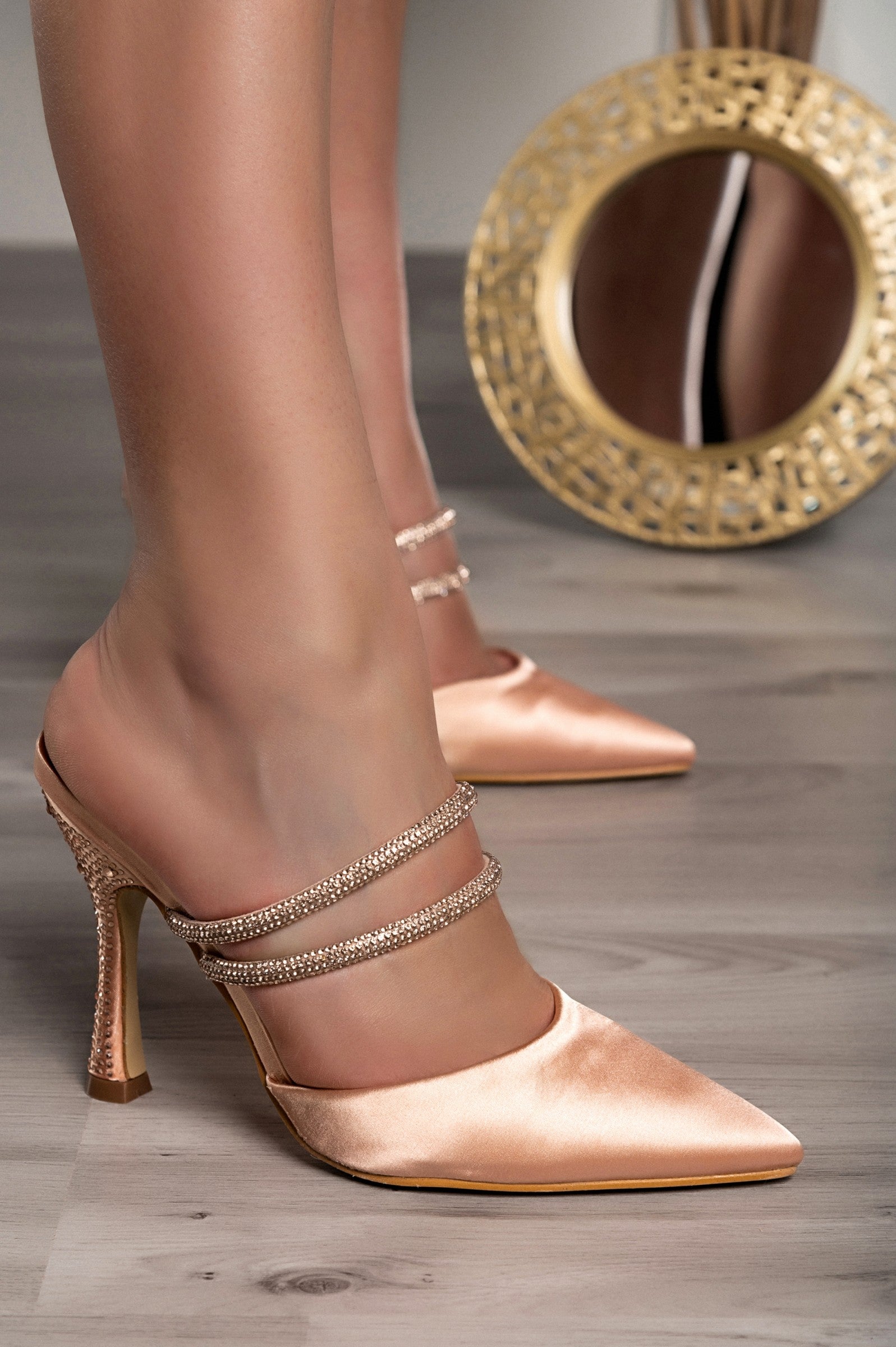 Beige heeled shoes with rhinestone straps and pointed toe design, featuring a thin heel for elegance.