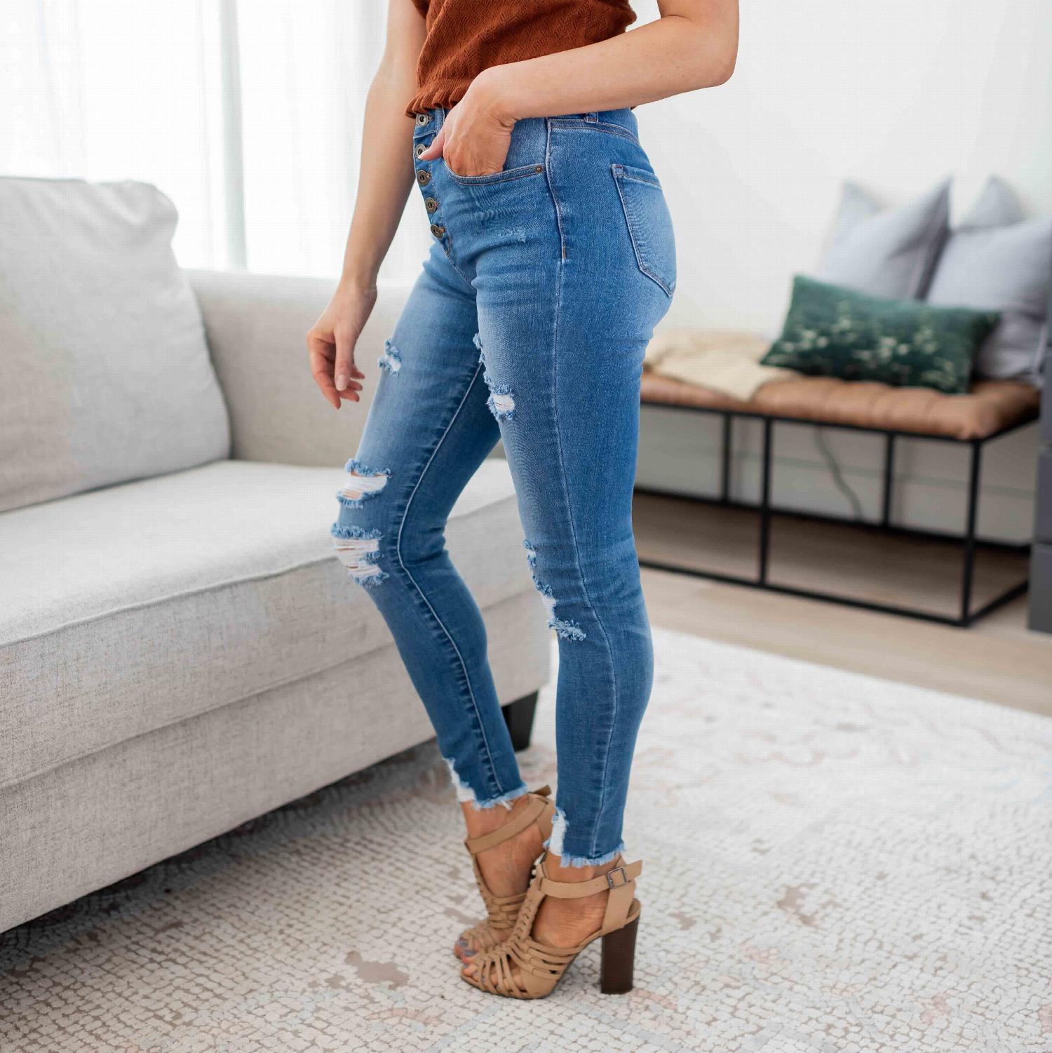 High-rise skinny destructed denim jeans with exposed button detailing, showcasing a stylish distressed look.