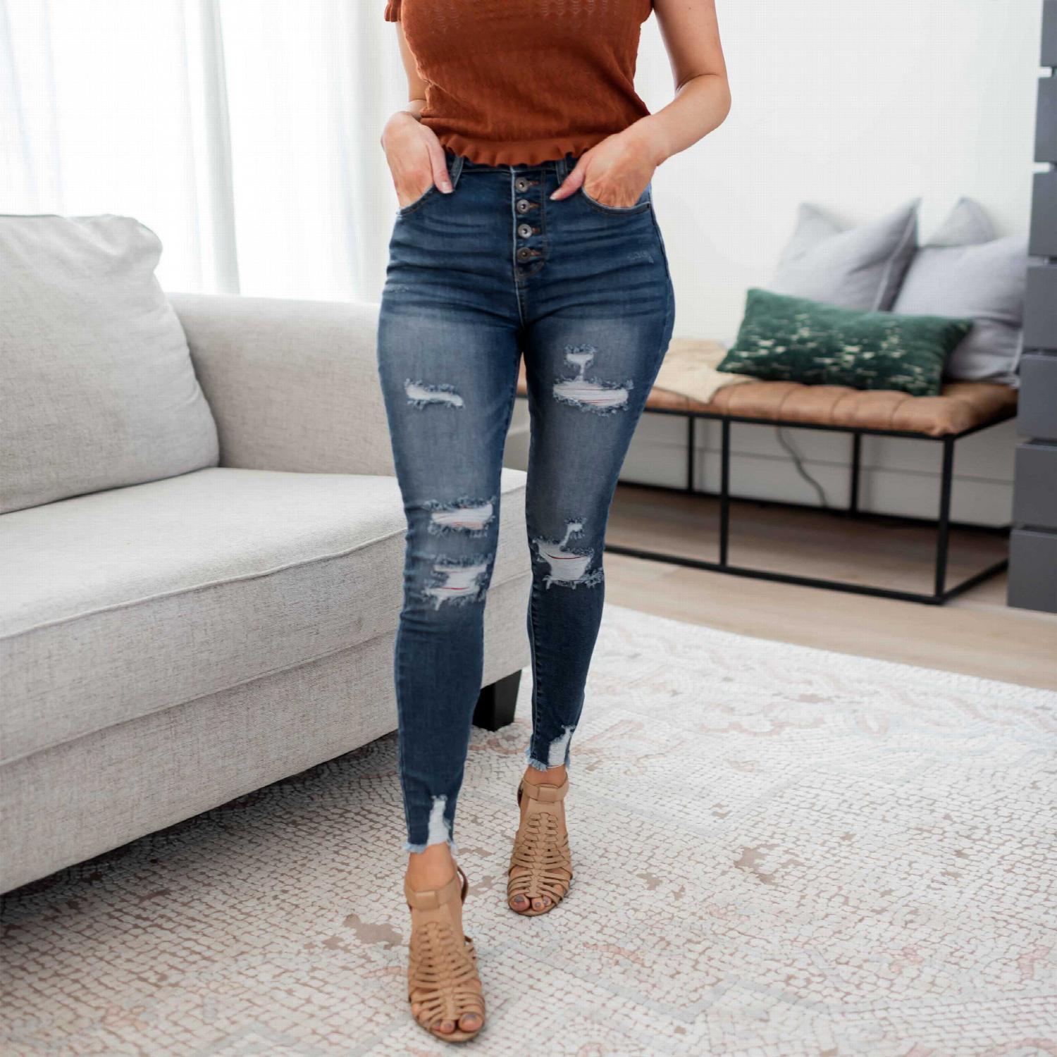 High-rise skinny destructed denim jeans with exposed button detailing, showcasing a stylish distressed look.