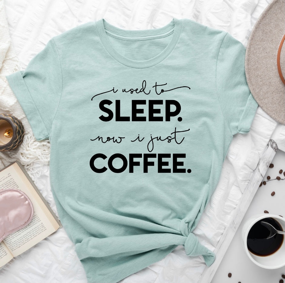 Heather dusty blue unisex t-shirt with 'I Used To Sleep Now I Just Coffee' printed in black ink, showcasing a stylish and comfortable design.