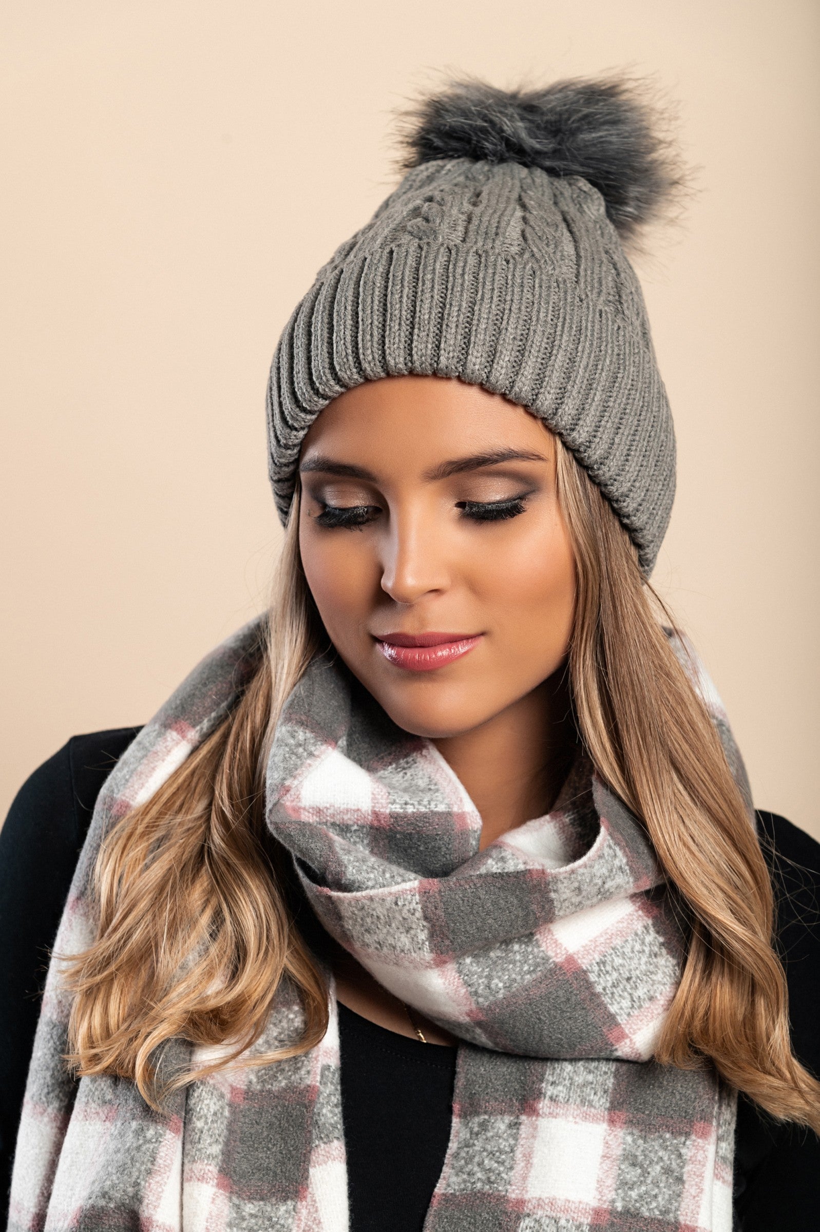 Dark gray knitted hat with a faux fur pompom on top, showcasing a rolled edge and ribbed knit design.