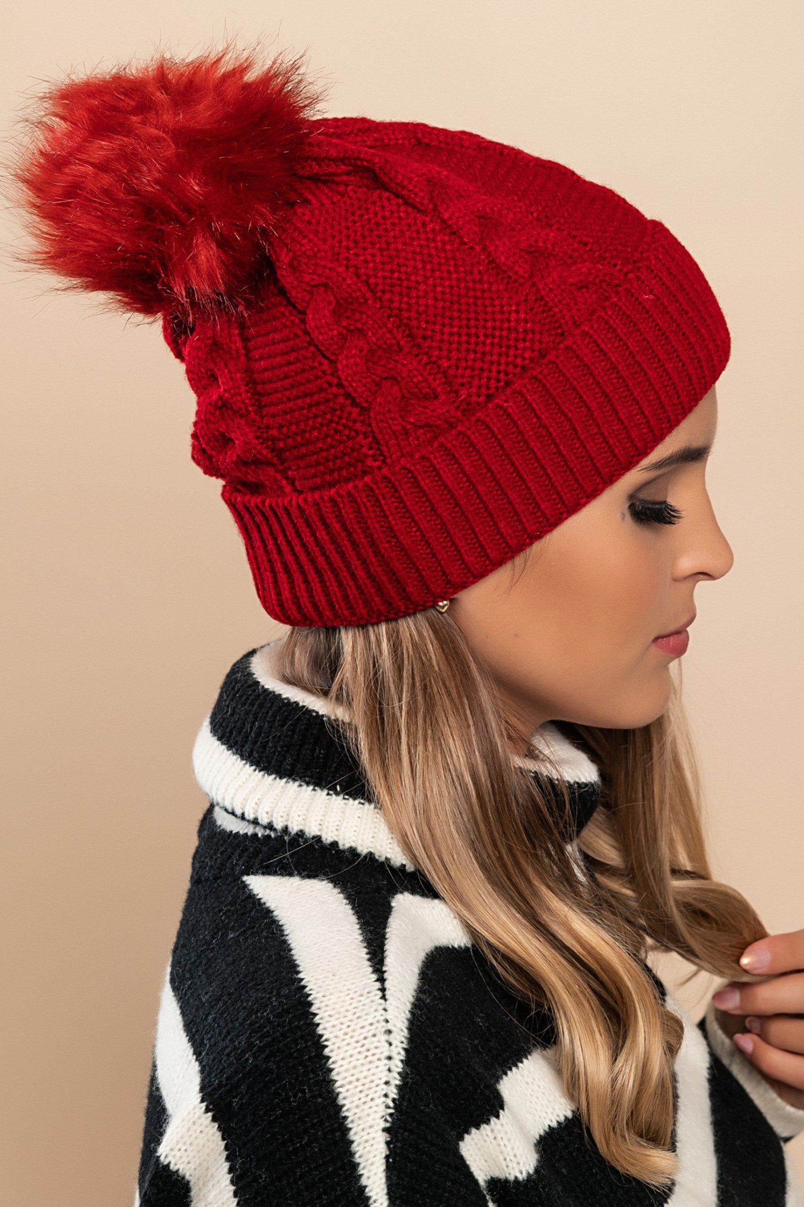 Burgundy knitted hat with a faux fur pompom on top, showcasing a rolled edge design.