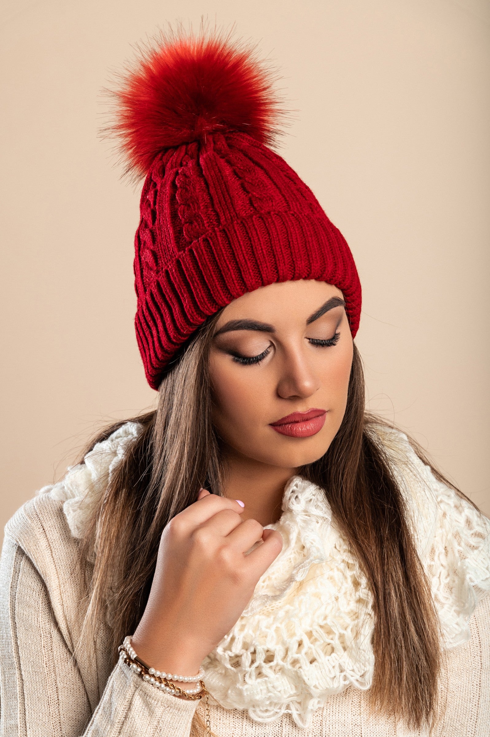 Burgundy knitted hat with a faux fur pompom, showcasing a rolled edge design and ribbed knit texture.