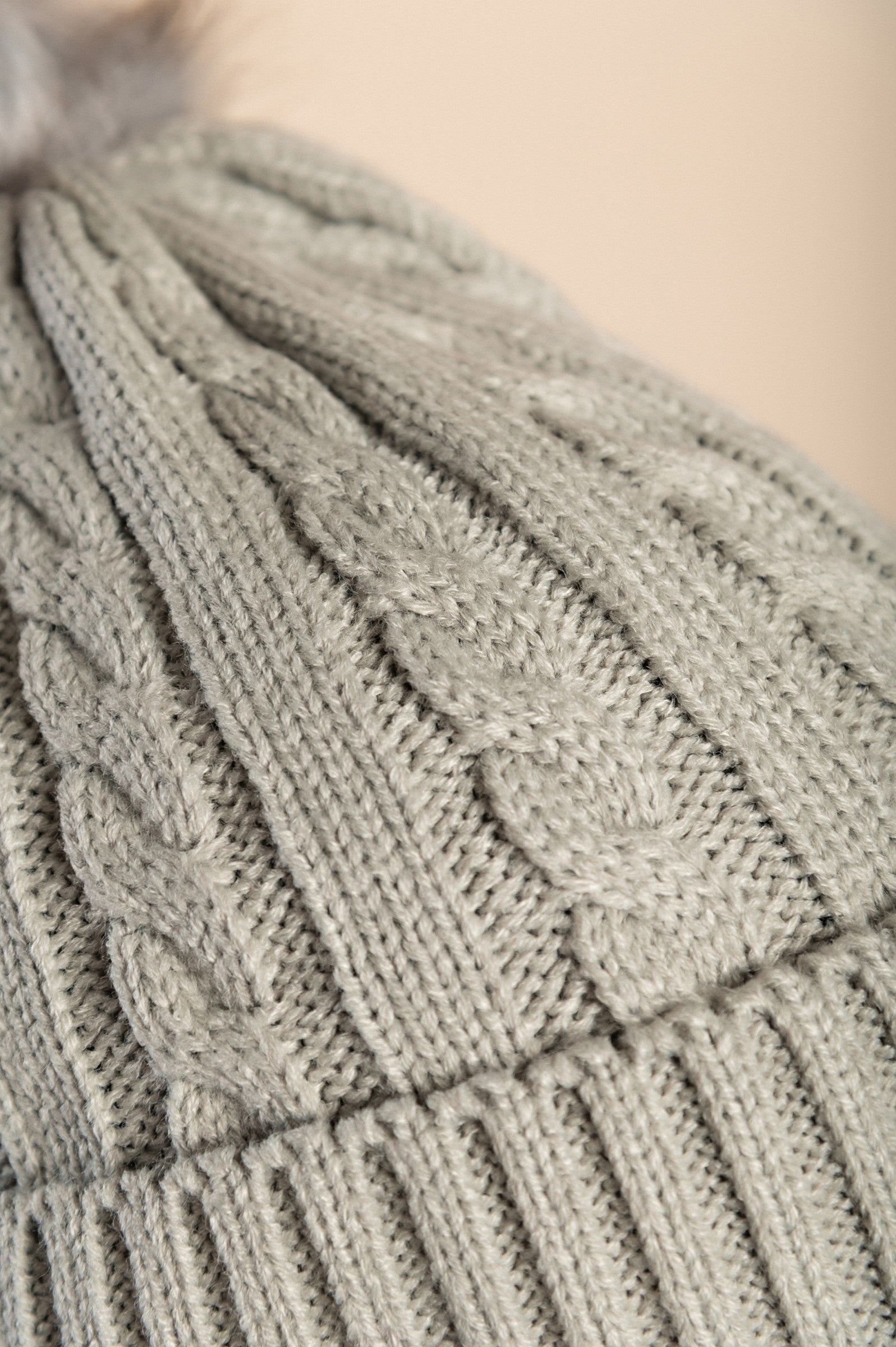 Light gray knitted hat with a faux fur pompom, showcasing a rolled edge and ribbed knit texture.