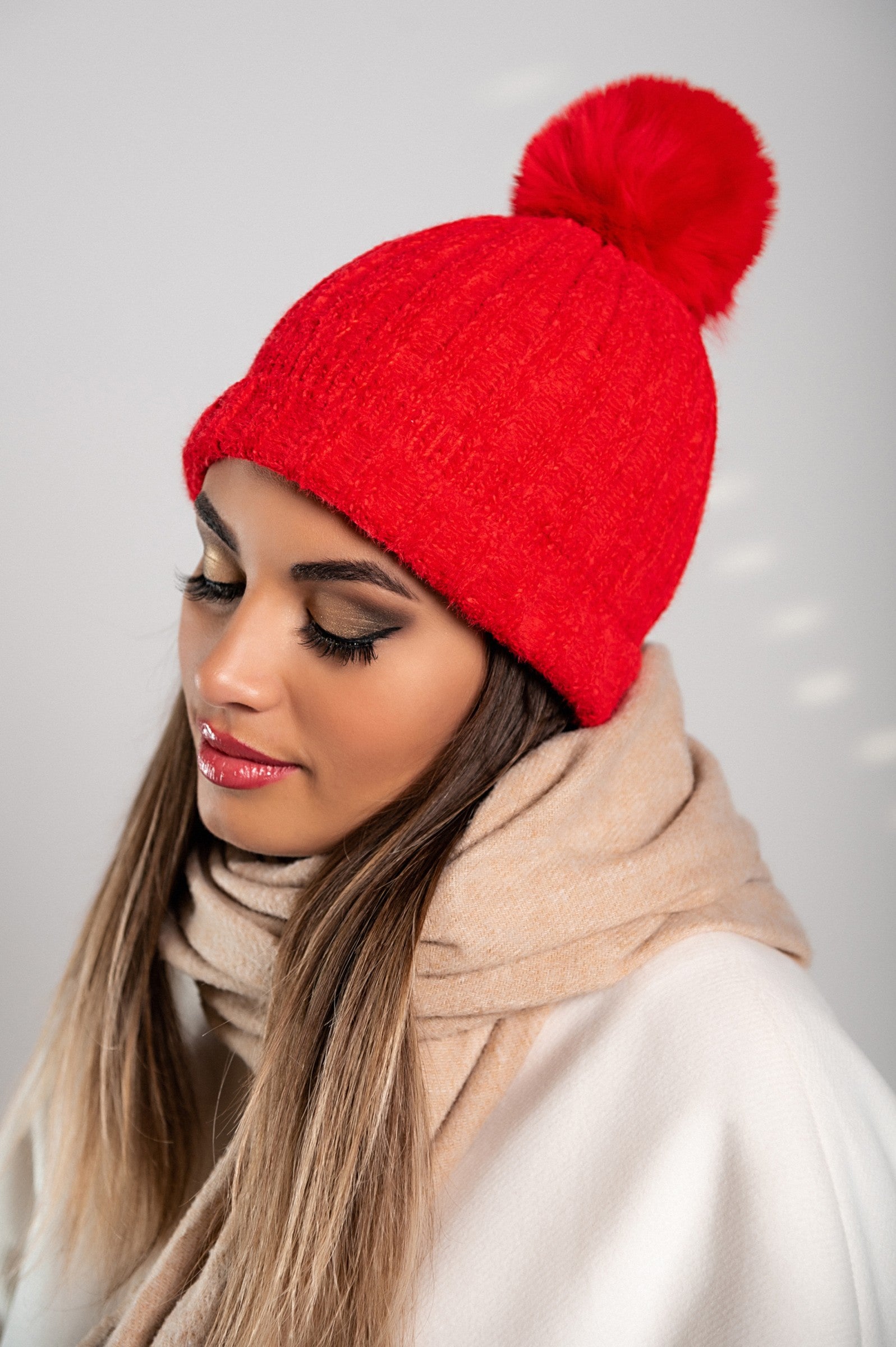 A vibrant red knitted hat with a decorative faux fur pompom, showcasing a ribbed knit design and a folded hem for added style.
