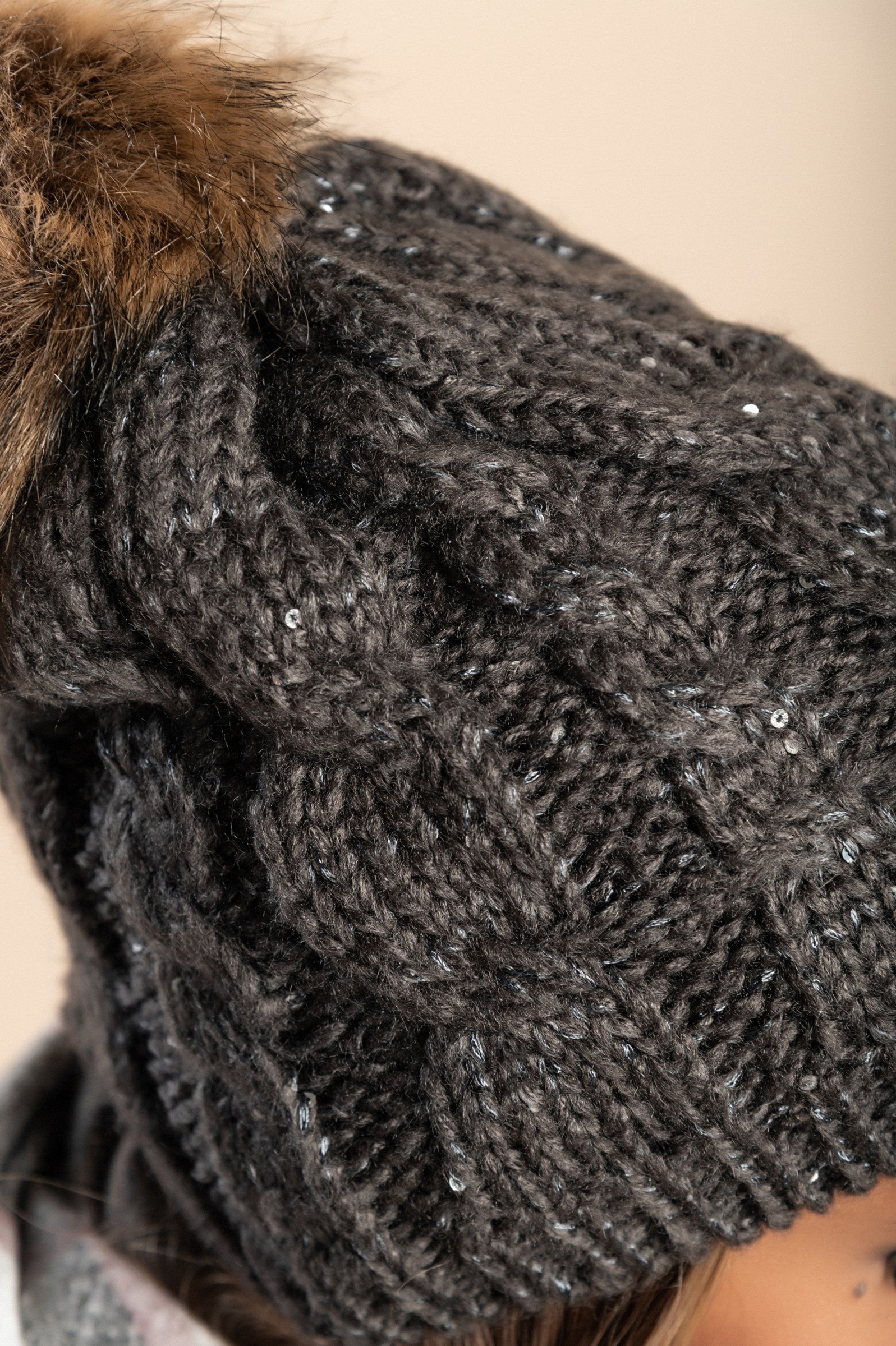 Gray knitted hat with sequins and faux fur pompom, showcasing a stylish ribbed knit design.