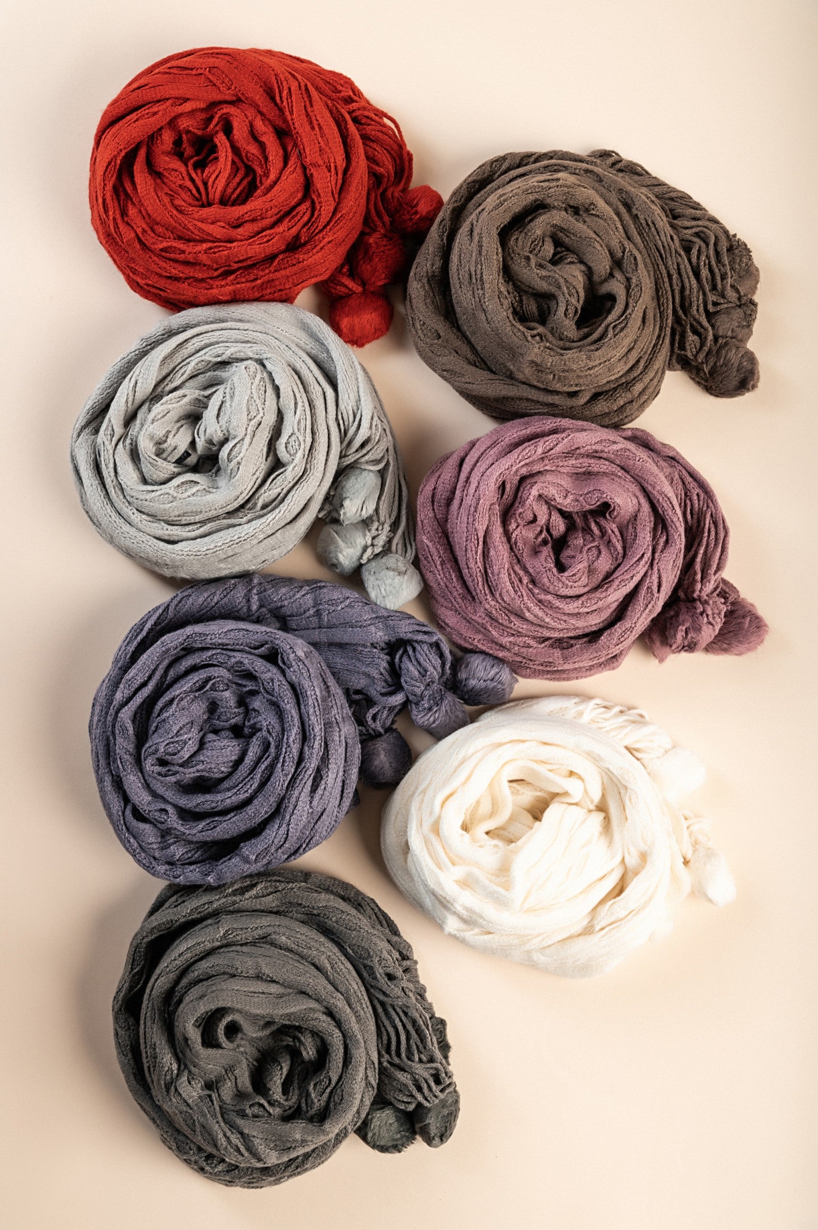 A colorful set of seven knitted scarves in various shades including white, dark gray, purple, pink, brown, and terracotta, showcasing their soft texture.