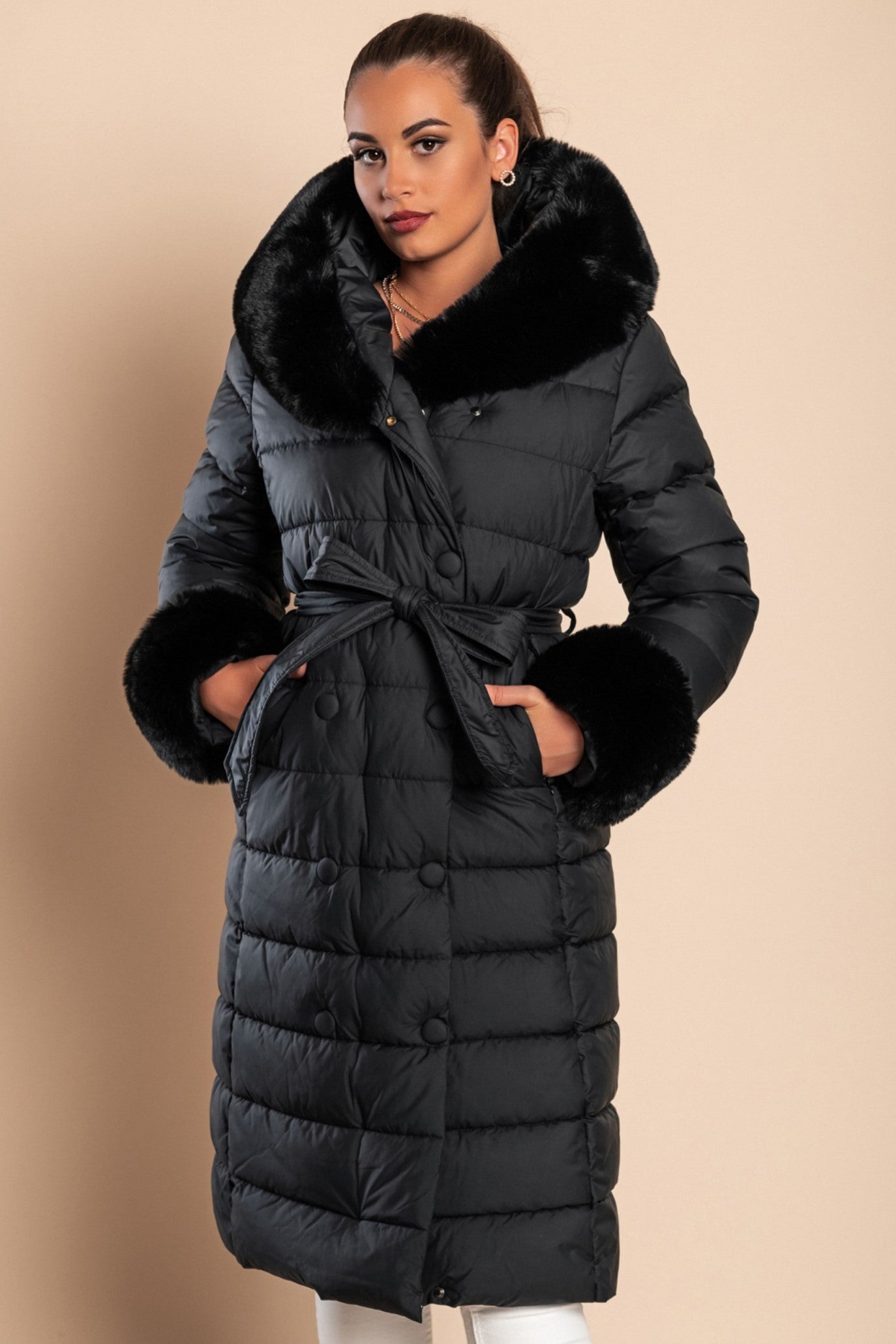 Long padded winter jacket in black with removable faux fur trim, side pockets, and decorative belt, designed for warmth and style.