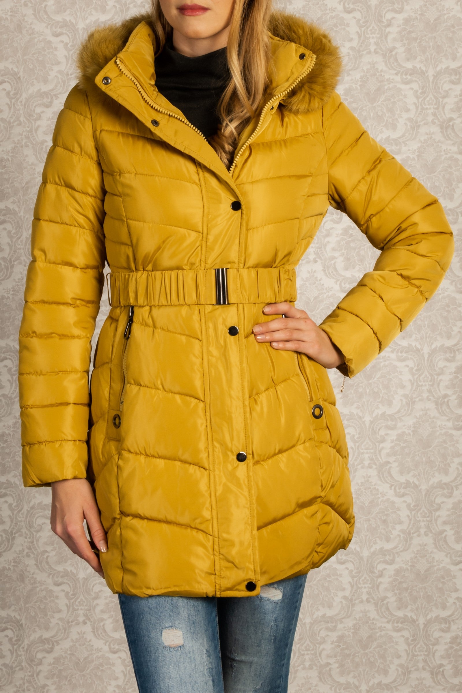 Long yellow quilted jacket with detachable faux fur hood, featuring zippered pockets and a waist belt.
