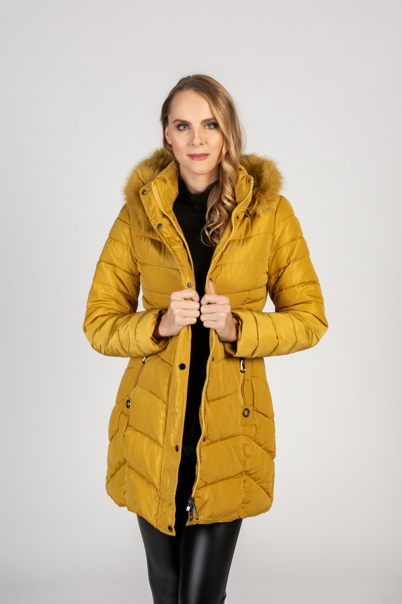 Long yellow quilted jacket with detachable faux fur hood, featuring zippered pockets and a waist belt.