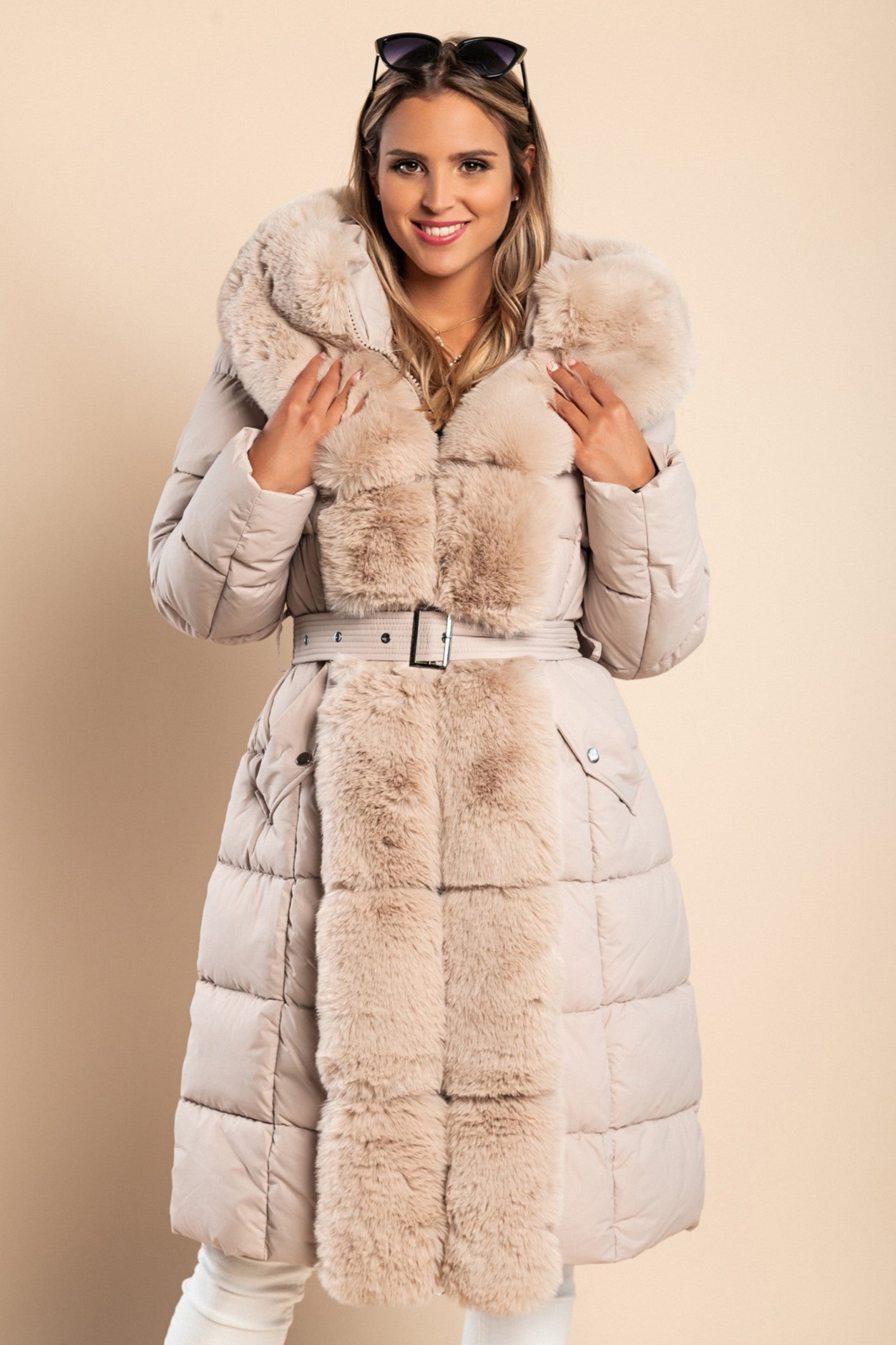 Beige padded winter jacket with removable faux fur hood, decorative belt, and side pockets.