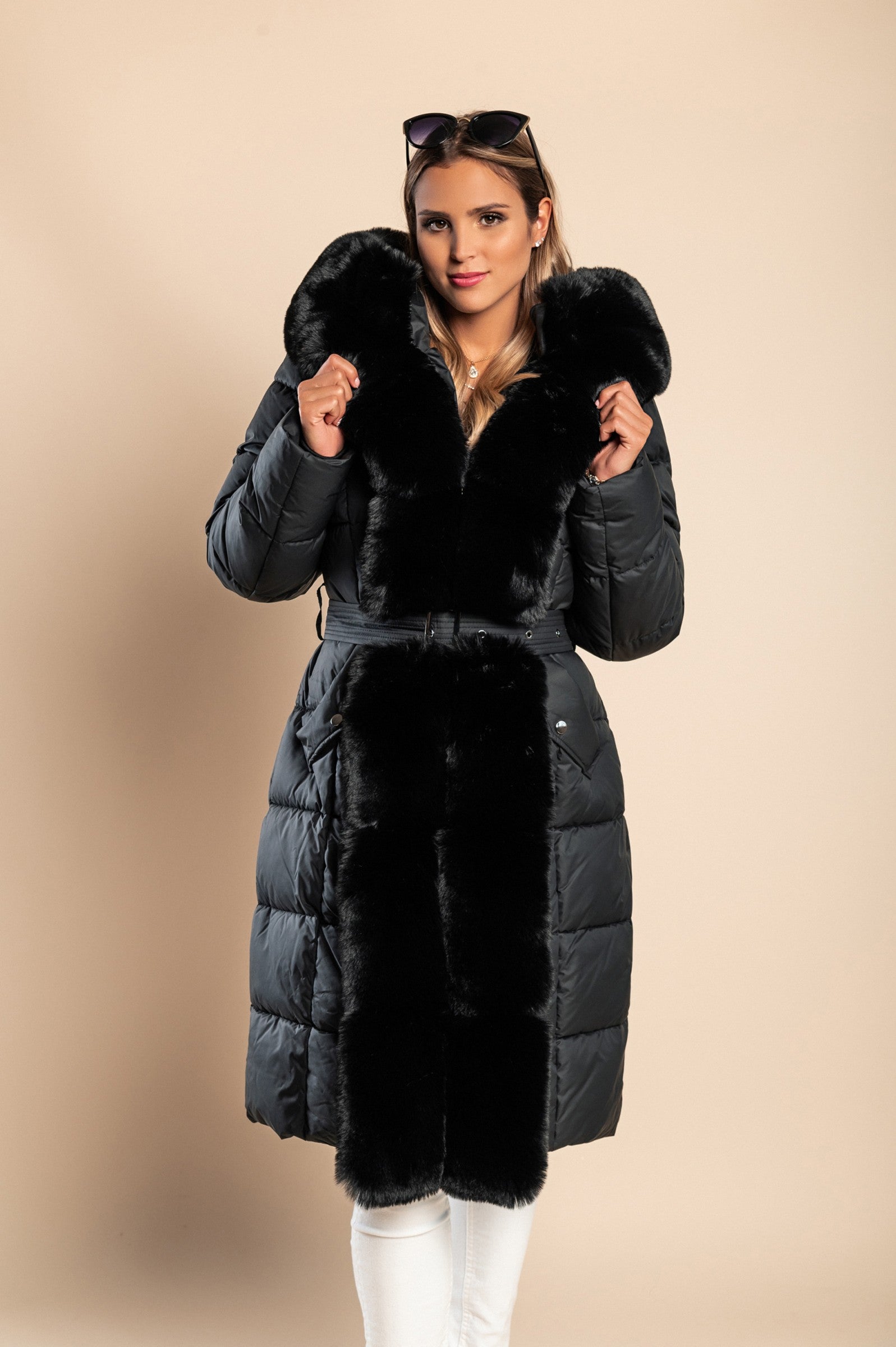 Padded winter jacket in black with removable faux fur hood and decorative belt, featuring side pockets and long sleeves.