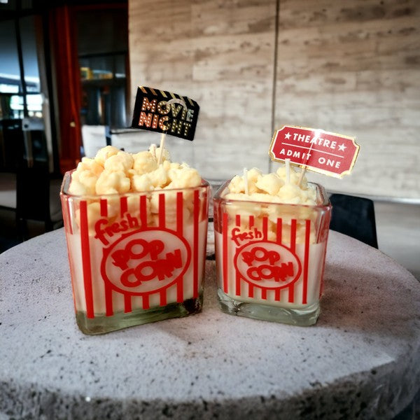 A cozy setup featuring popcorn theme scented soy wax candles in 10 oz and 16 oz sizes, perfect for movie nights.