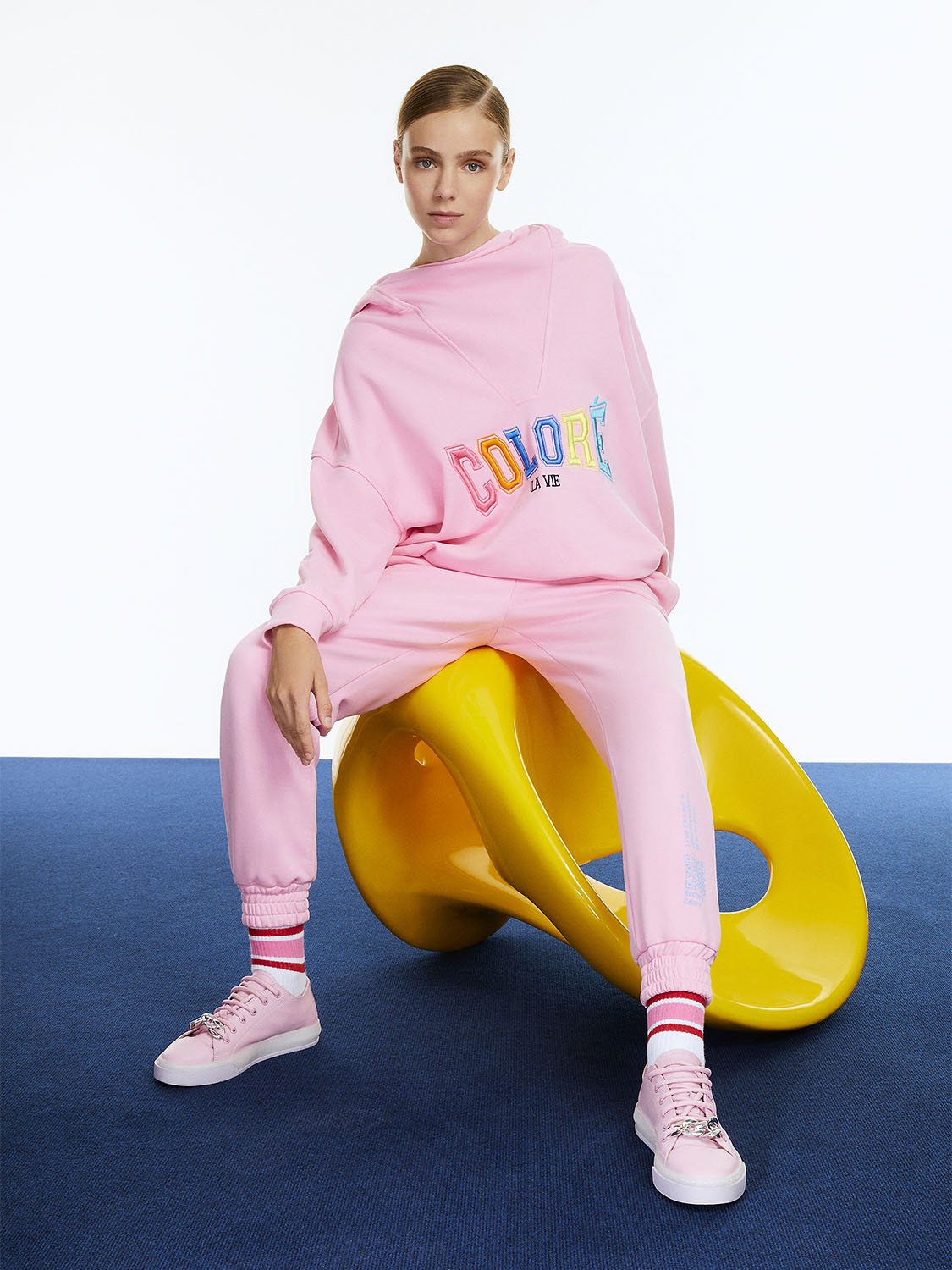 A pair of high-waisted ankle-length printed jogging pants featuring an elastic waistband and vibrant colors of orange, pink, and blue.