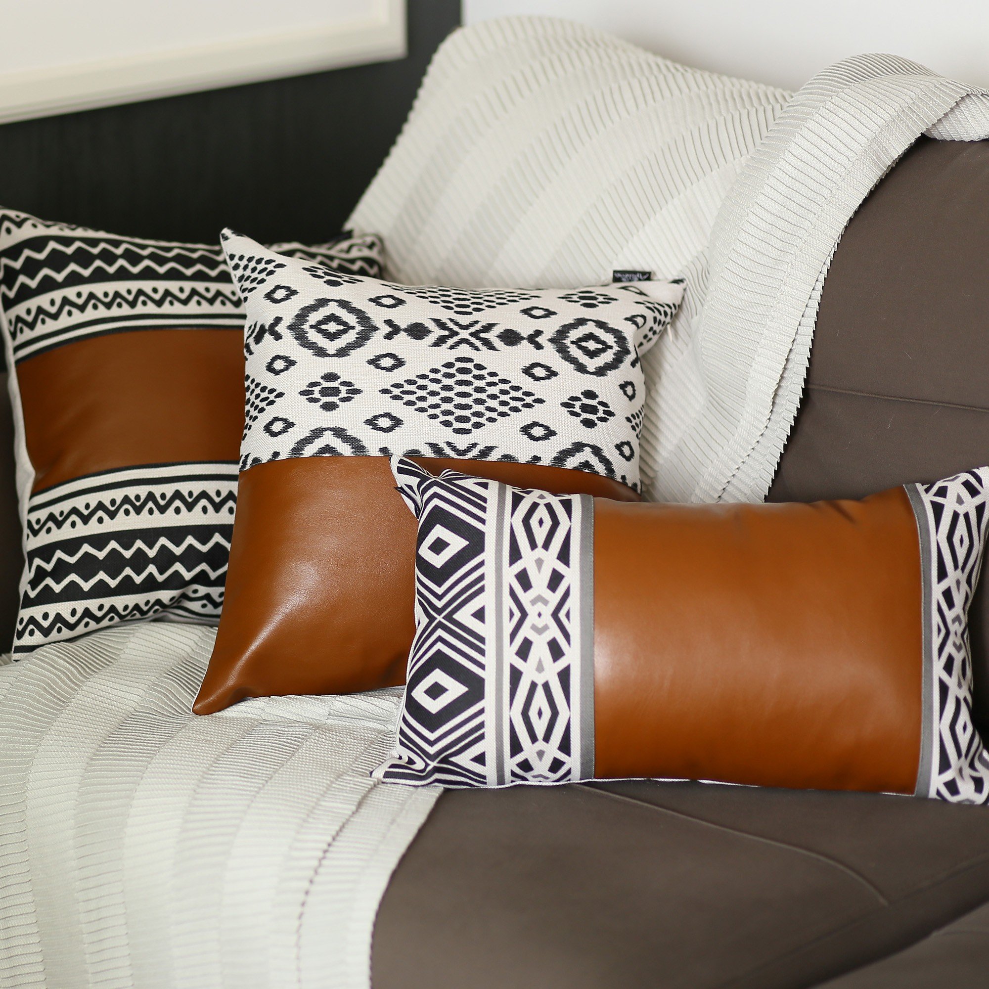 Rectangular lumbar pillow cover in rustic brown faux leather with geometric patterns in charcoal black and daisy white, featuring a hidden zipper.