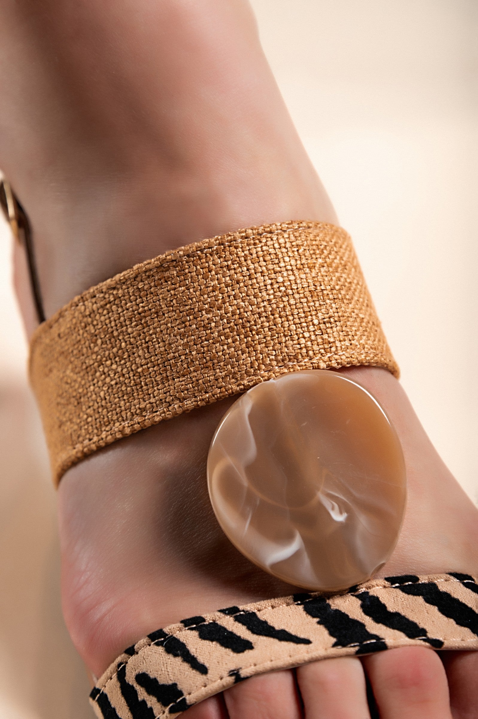 Beige and zebra patterned flat-soled sandals with decorative details and ankle strap.