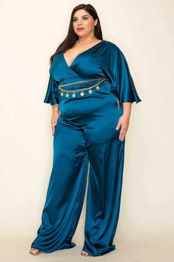 A teal satin jumpsuit featuring a wrap front, short sleeves, and a smocked waist, complemented by a stylish chain belt.
