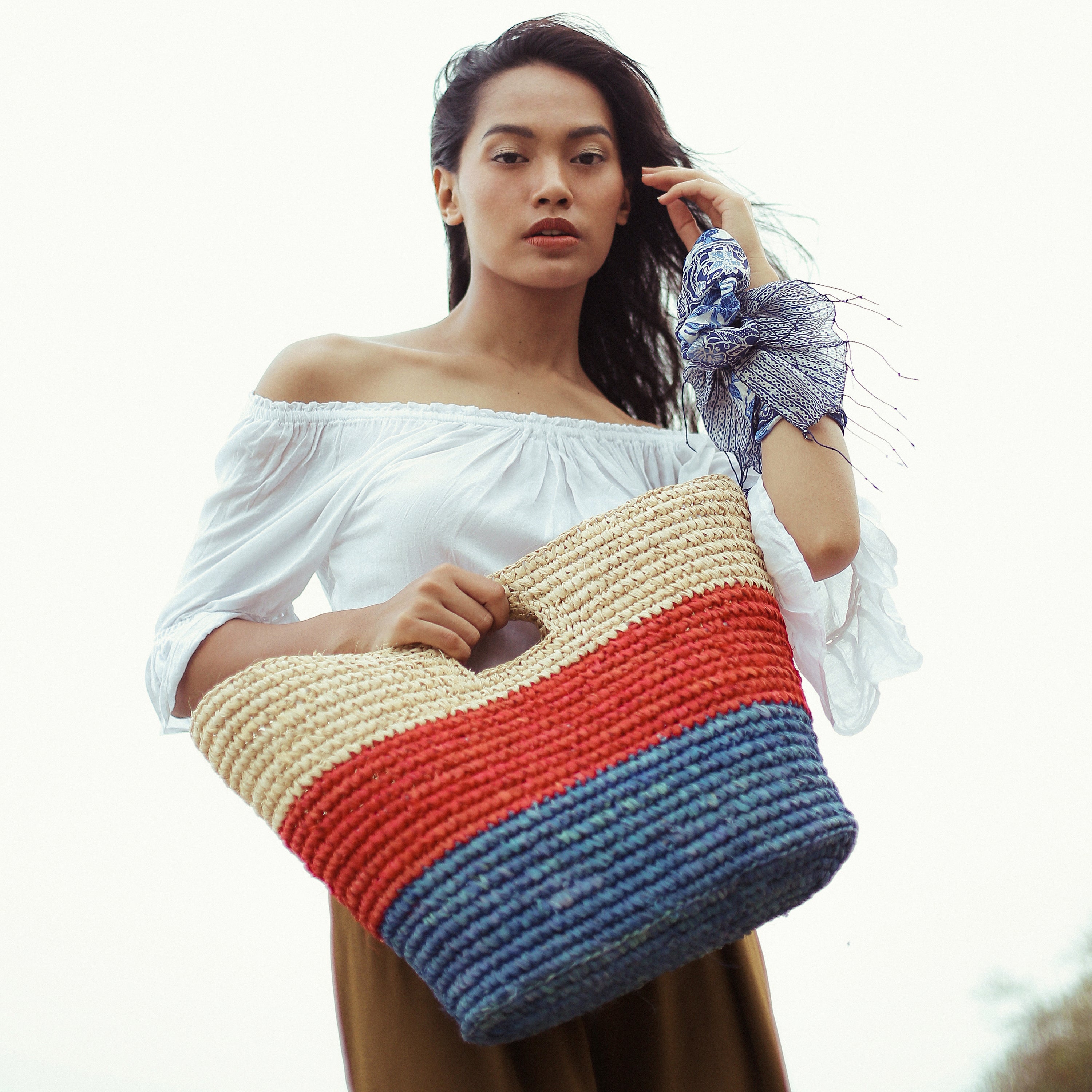 SAYAN Raffia Tote Bag in vibrant red and blue, handcrafted from natural raffia straws, perfect for beach outings.