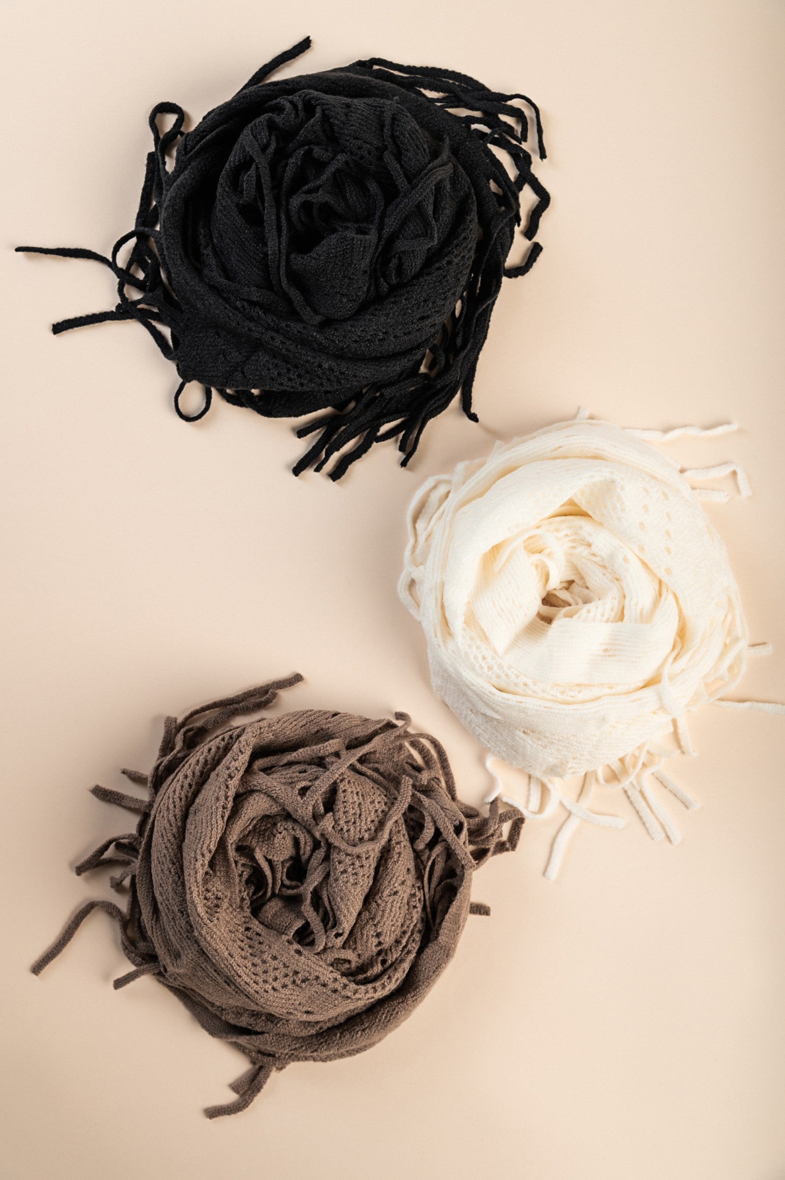 Set of three knitted scarves in white, black, and beige with fringes, displayed elegantly.