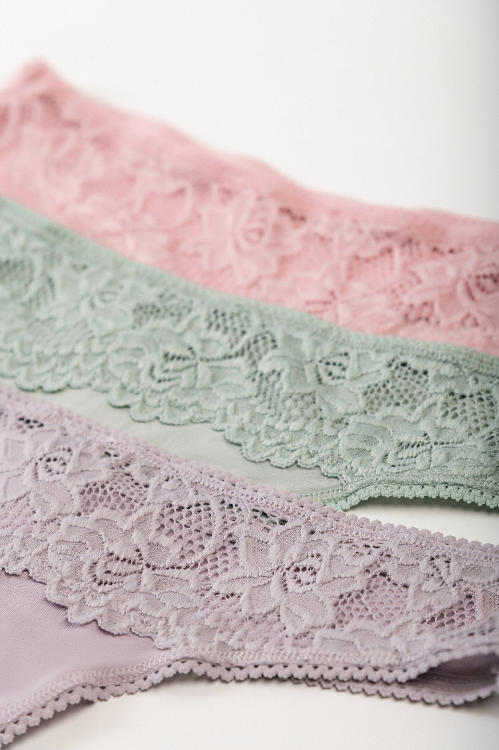 Set of three cotton thongs with lace in grey, light pink, and light green colors, showcasing their elegant design and comfortable fit.