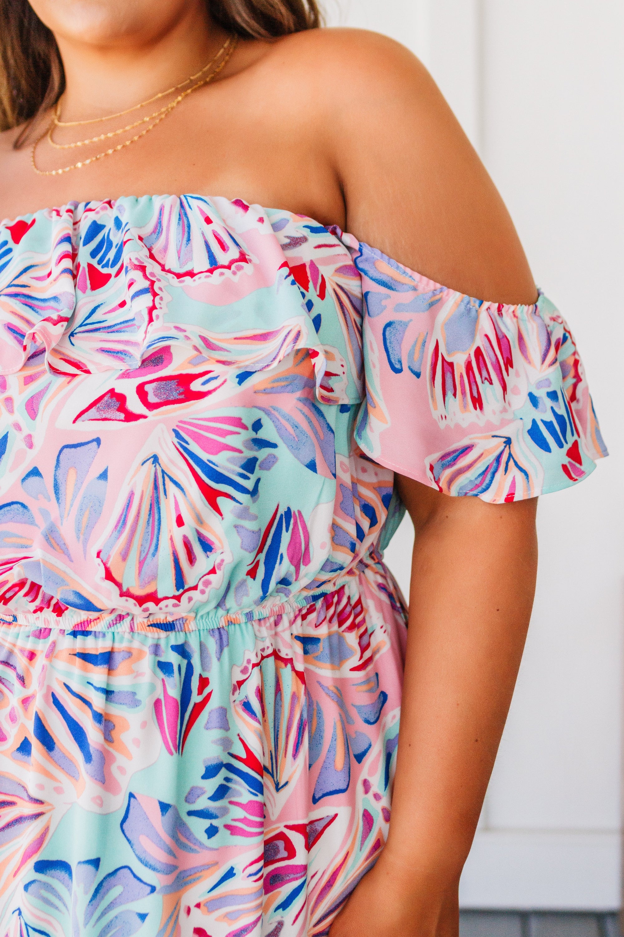 A beautiful model wearing the She Sells Sea Shells Maxi Dress featuring a ruffled neckline and asymmetrical hem in a breezy shell print.