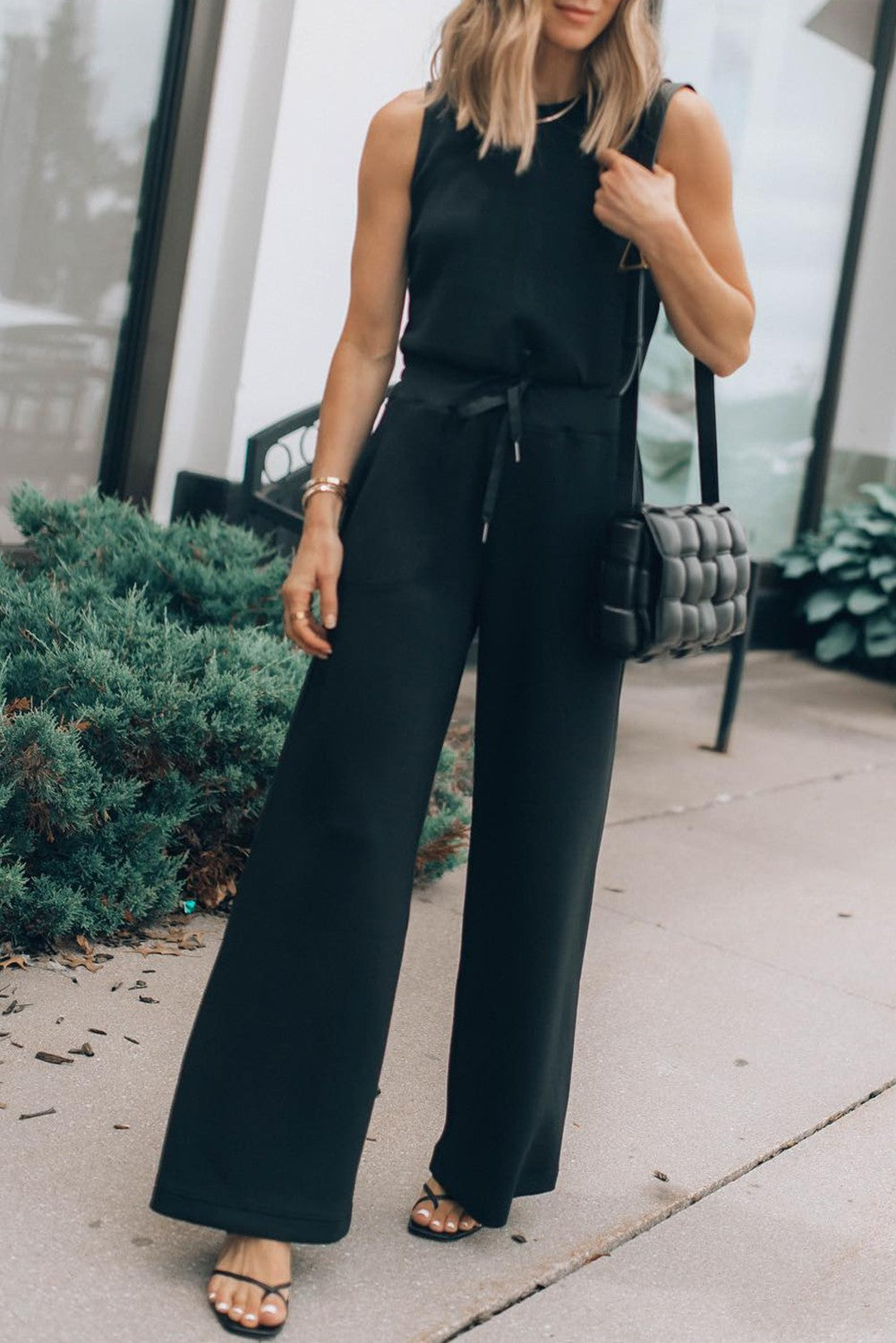A stylish black sleeveless jumpsuit featuring a round neckline and drawstring waist, with long loose pants, perfect for various occasions.