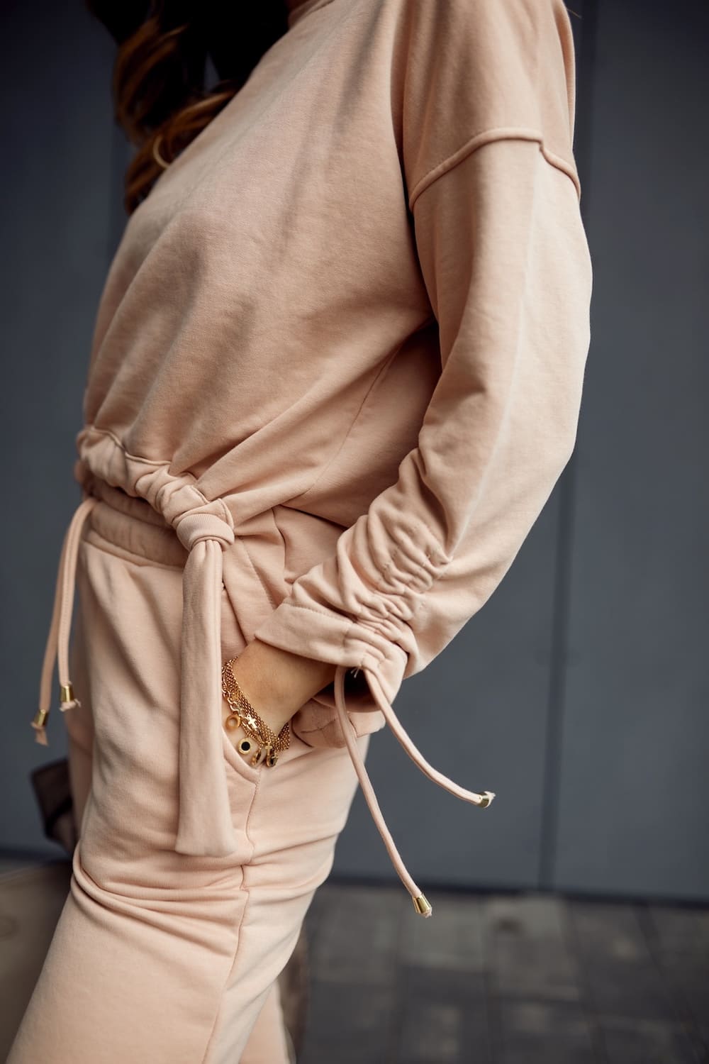 Beige women's tracksuit featuring an asymmetric sweatshirt and tapered pants, showcasing a stylish and comfortable design.