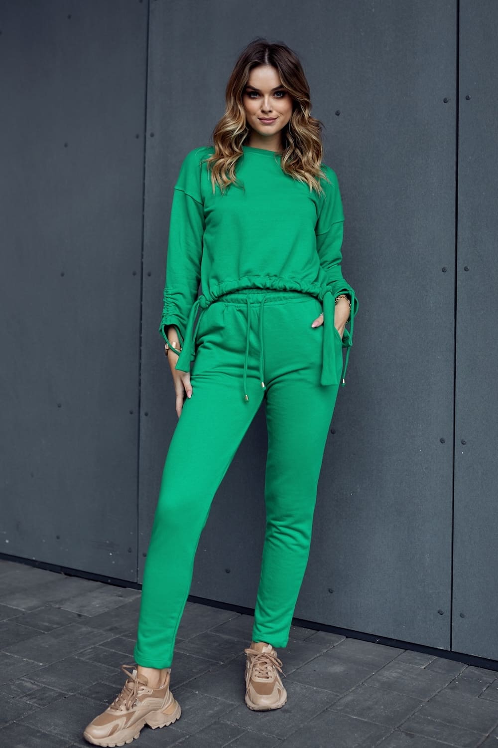 Smooth women's tracksuit featuring an asymmetric sweatshirt in green, showcasing a loose fit and tapered pants with pockets.