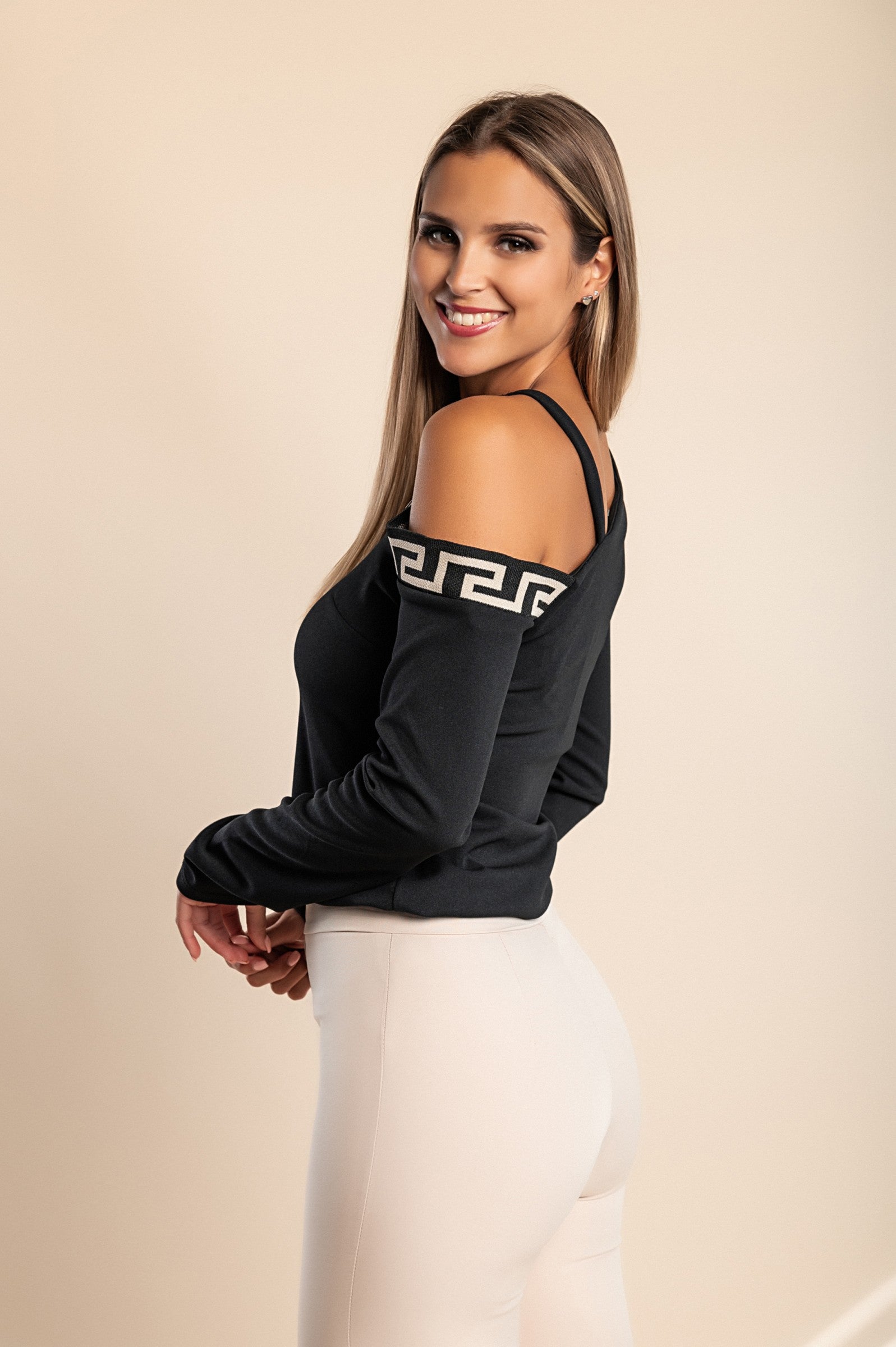 Stylish black top featuring a geometric print, asymmetrical neckline, metallic strap details, and long sleeves, perfect for any occasion.