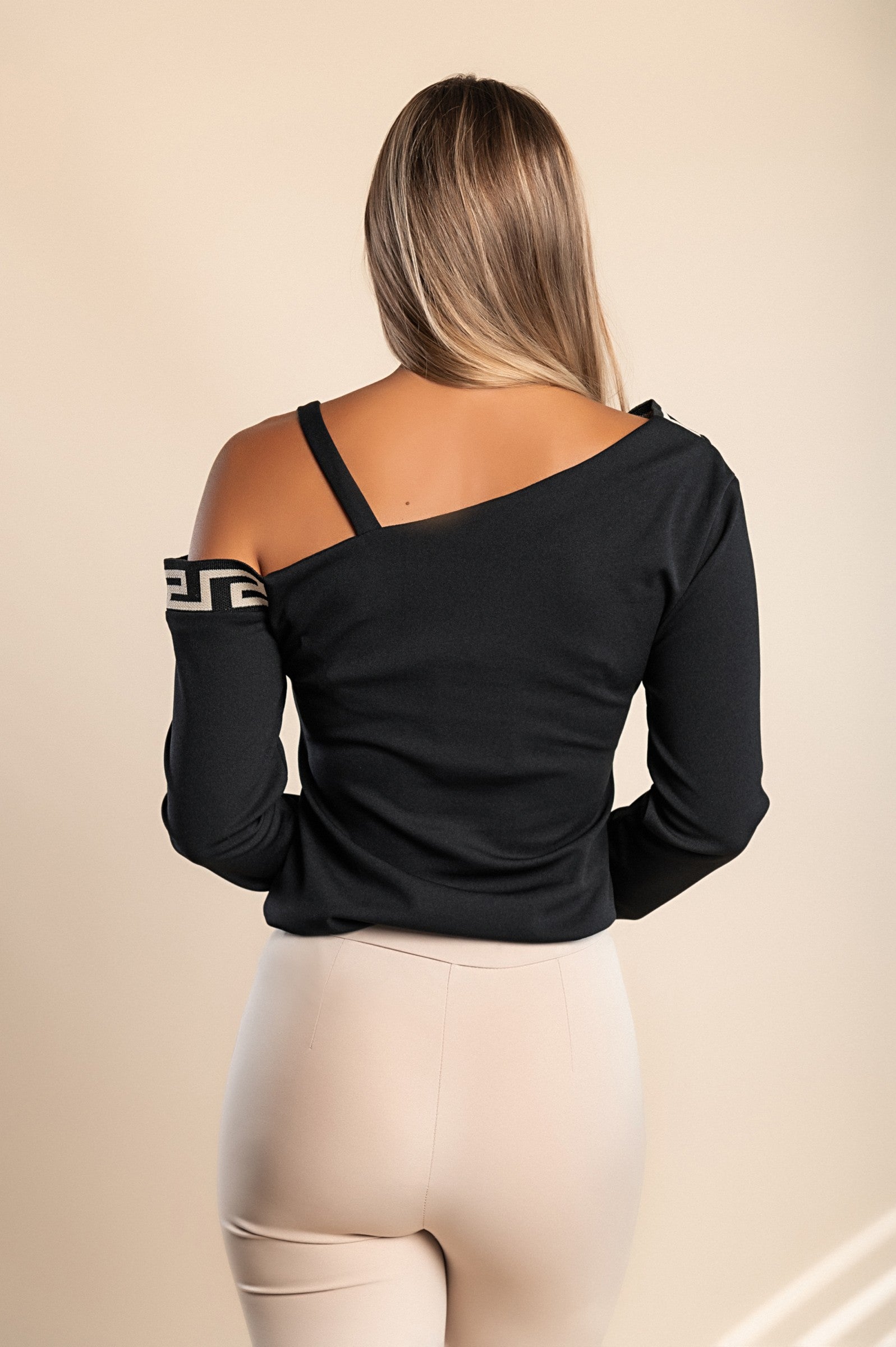 Stylish black top featuring a geometric print, asymmetrical neckline, metallic strap details, and long sleeves, perfect for any occasion.