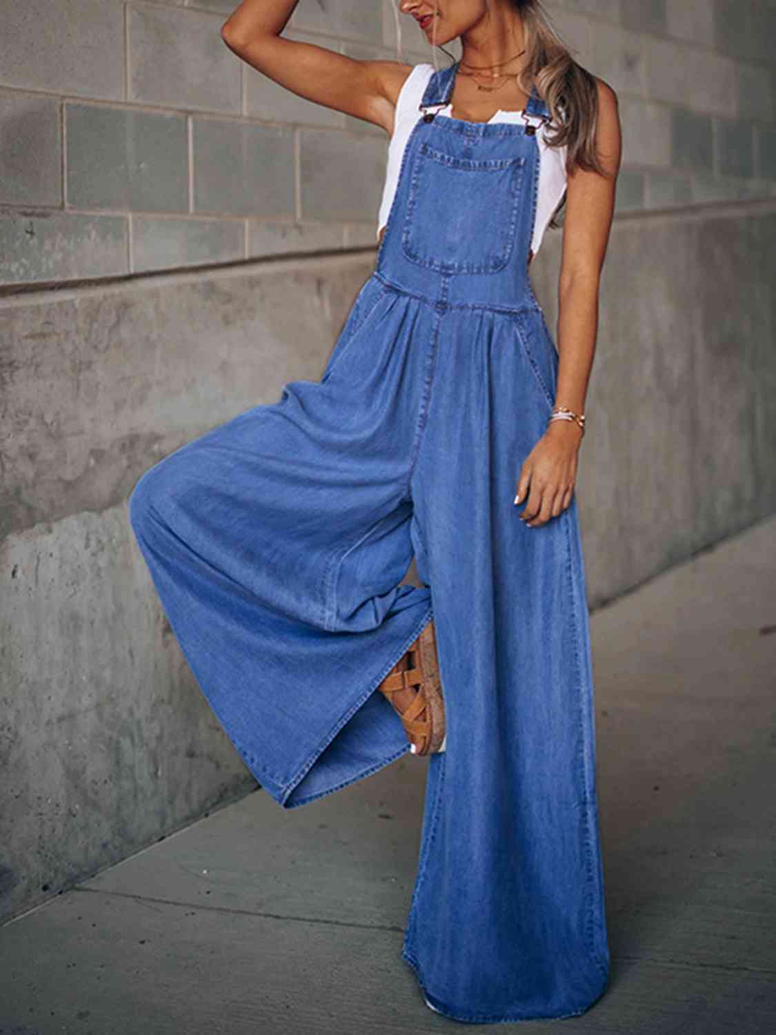 Wide leg denim overalls in a classic blue color, featuring adjustable straps and a relaxed fit, perfect for casual wear.