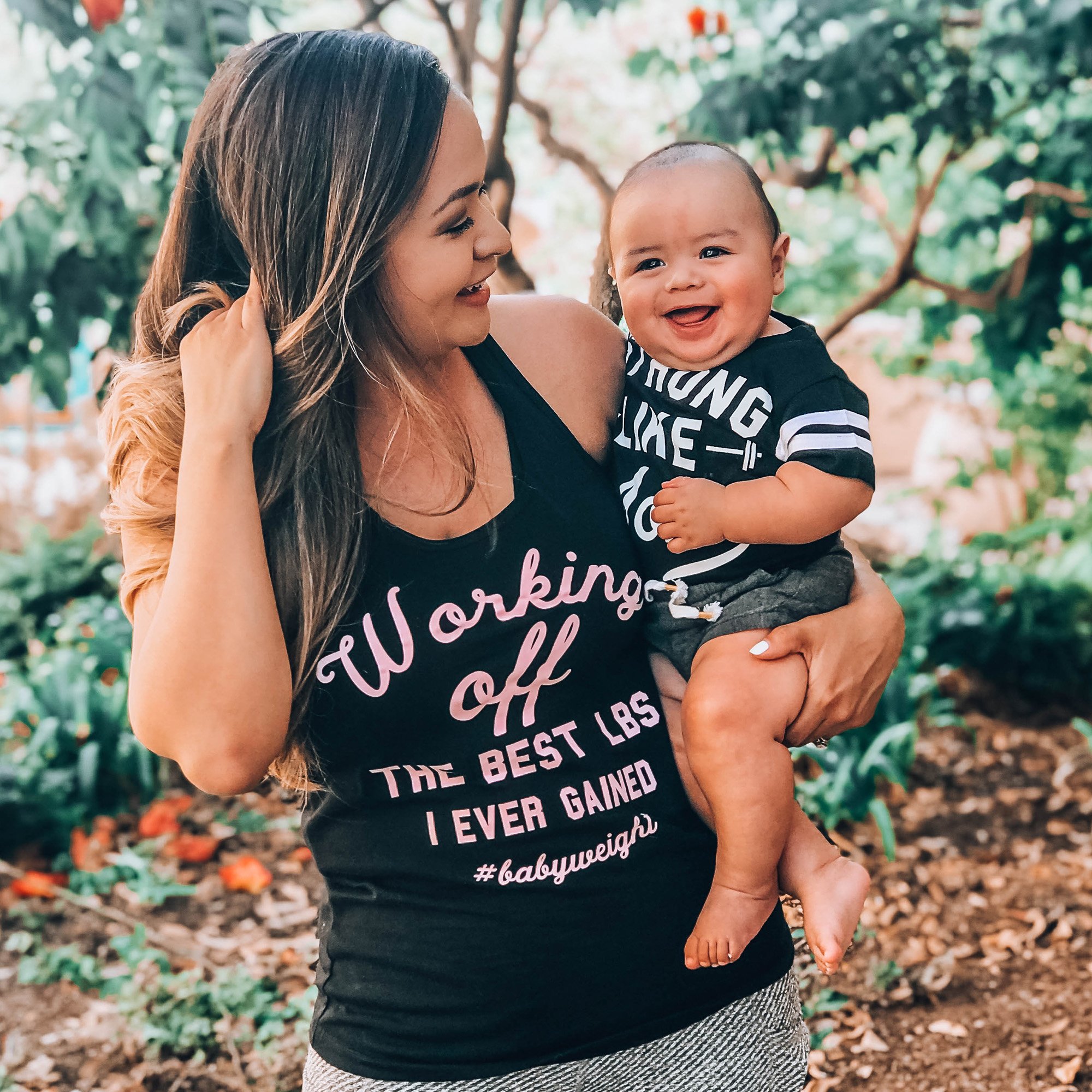 Black racerback tank top with light pink print saying 'Working off the best lbs I ever gained #babyweight', designed for moms.
